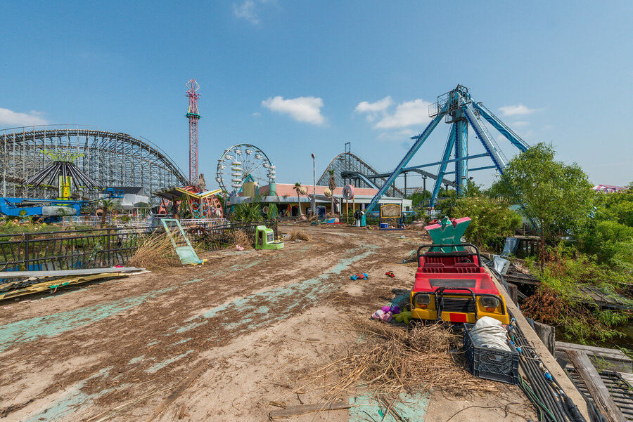 Atmospheric fine art photograph of abandoned roller coaster tracks rising above an overgrown New Orleans landscape, dramatic sky overhead