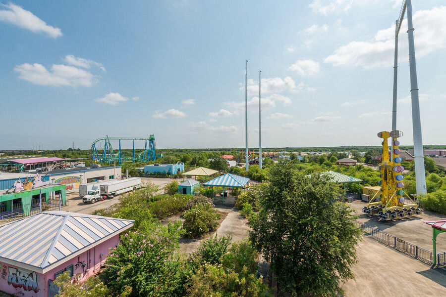 Atmospheric fine art photograph of abandoned roller coaster tracks rising above an overgrown New Orleans landscape, dramatic sky overhead