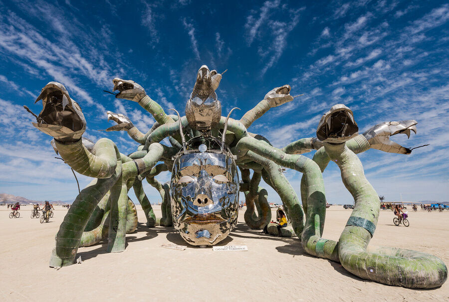 Documentary fine art photograph of a Burning Man installation at sunset, sculptural form casting long shadows across the alkali flat