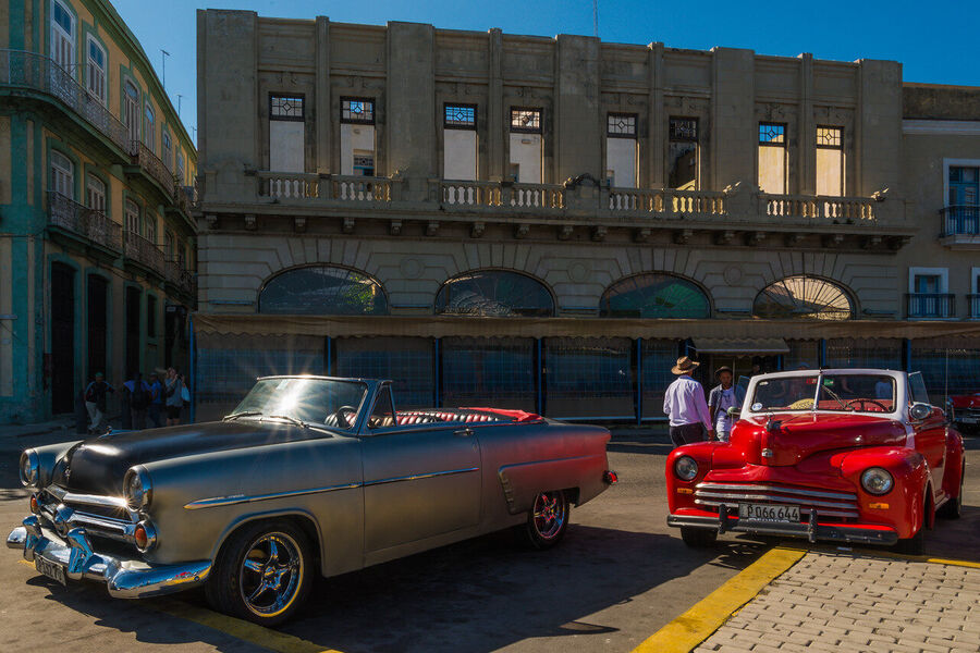 Fine art documentary photograph of a vintage American automobile on Havana's Malecón seawall at golden hour, warm Caribbean light on chrome