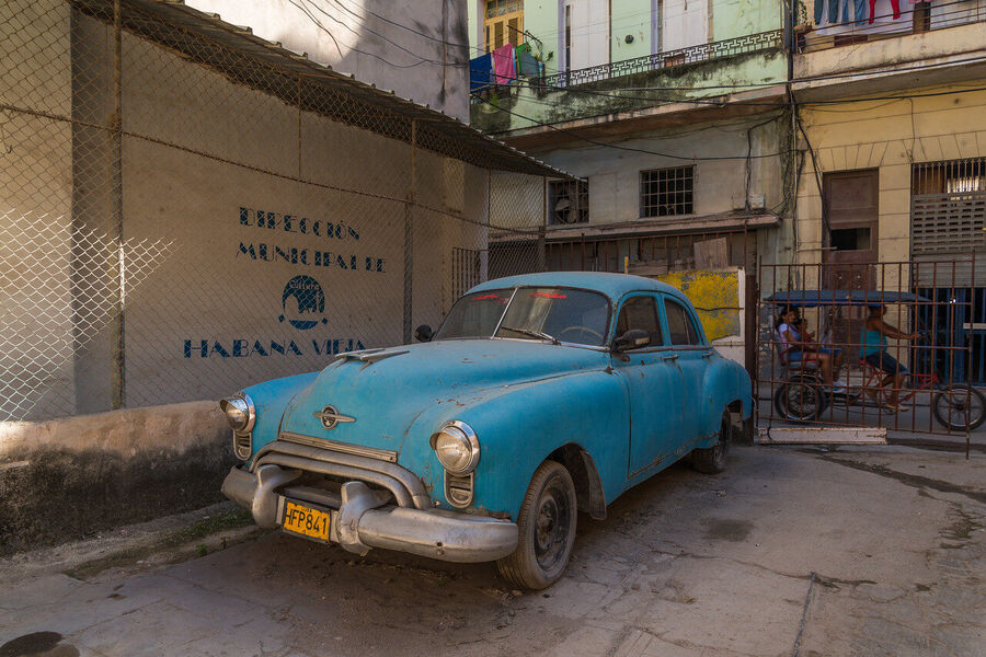 Fine art documentary print of a Havana musician performing in a sun-drenched colonial courtyard, dappled light falling across warm terracotta walls