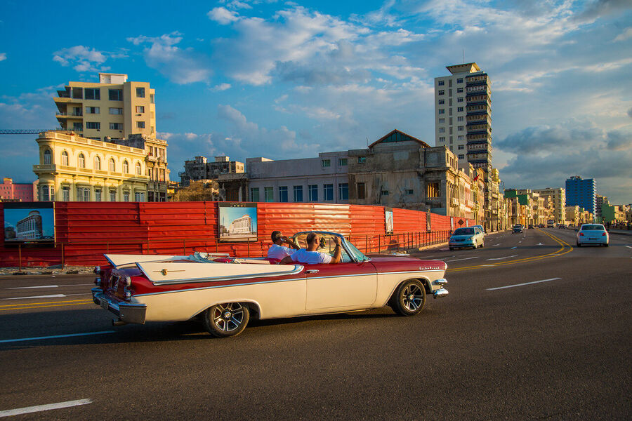 Fine art documentary photograph of a vintage American automobile on Havana's Malecón seawall at golden hour, warm Caribbean light on chrome
