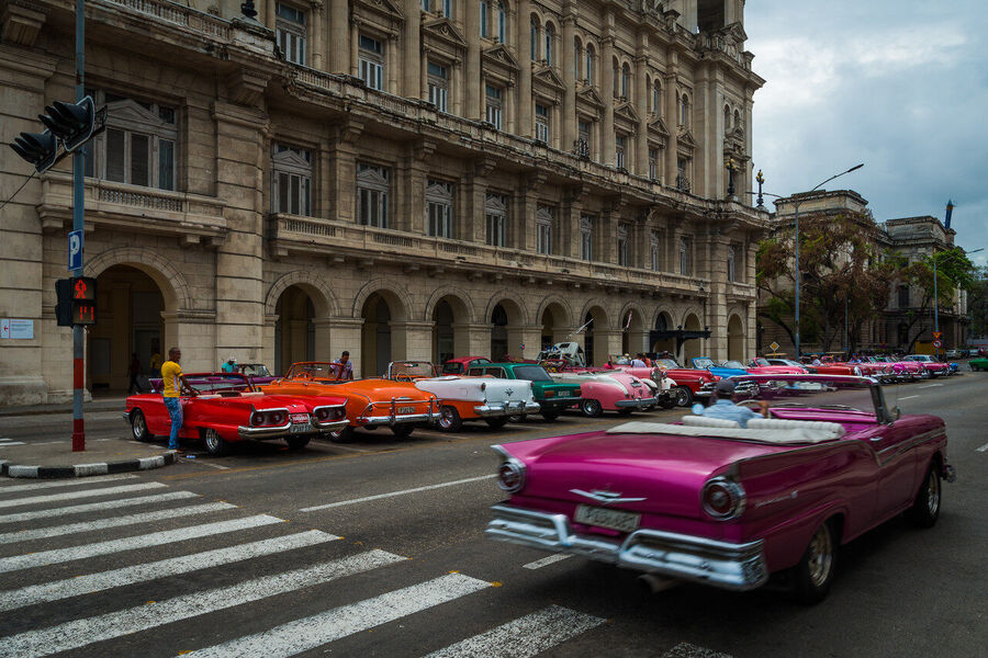 Fine art documentary photograph of a vintage American automobile on Havana's Malecón seawall at golden hour, warm Caribbean light on chrome
