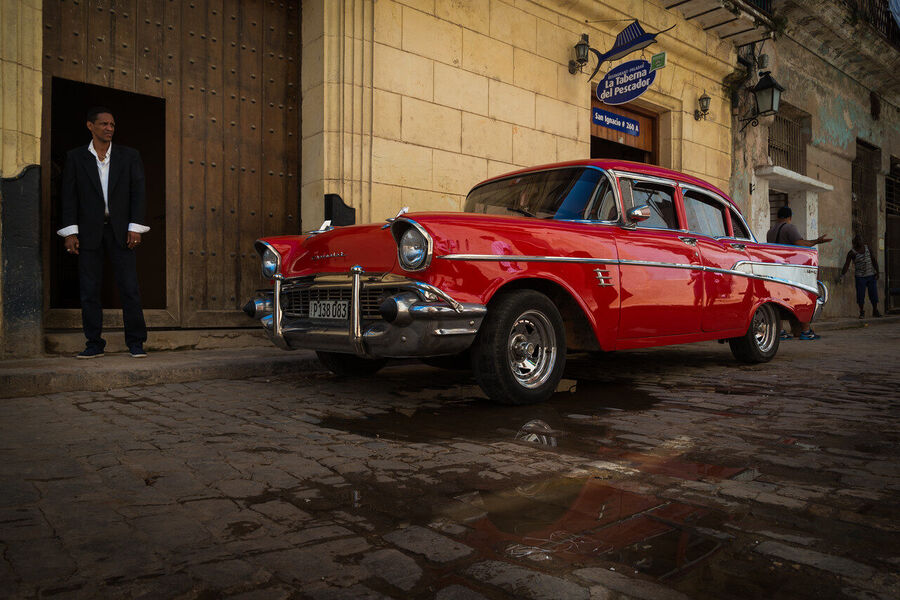 Fine art documentary print capturing everyday Havana life — a quiet street scene of extraordinary human warmth and architectural grandeur