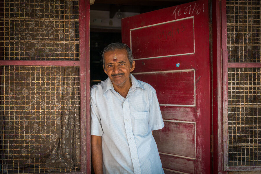 Fine art portrait print of an Indian holy man at dawn, soft ambient light from a temple doorway creating a near-painterly quality