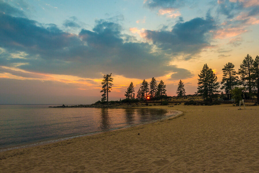 Wide angle fine art landscape print of Lake Tahoe's granite shoreline at golden hour, Sierra Nevada peaks faintly visible through warm atmospheric haze