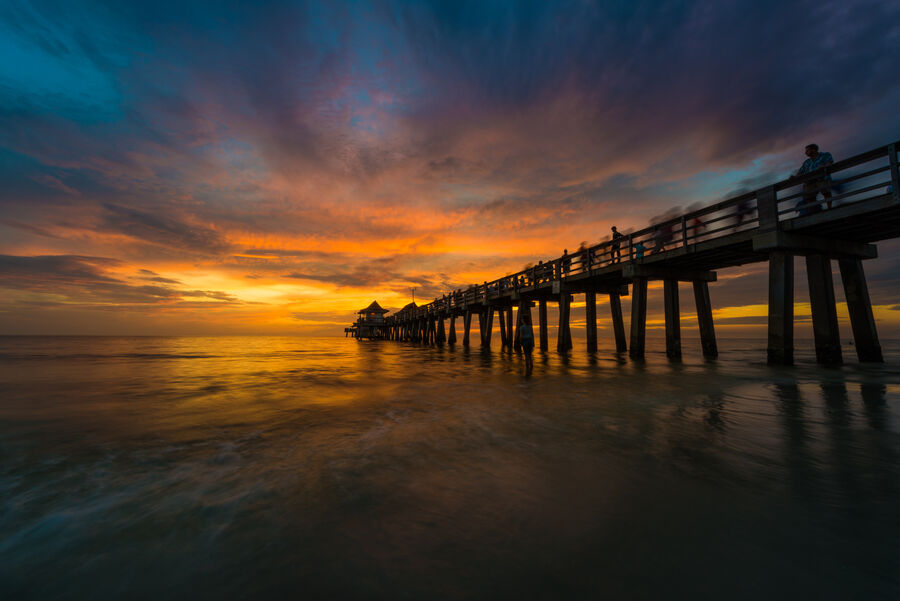 Fine art photograph of a Naples sunset reflected in the wet sand at low tide, the pier structure extending to the right of frame