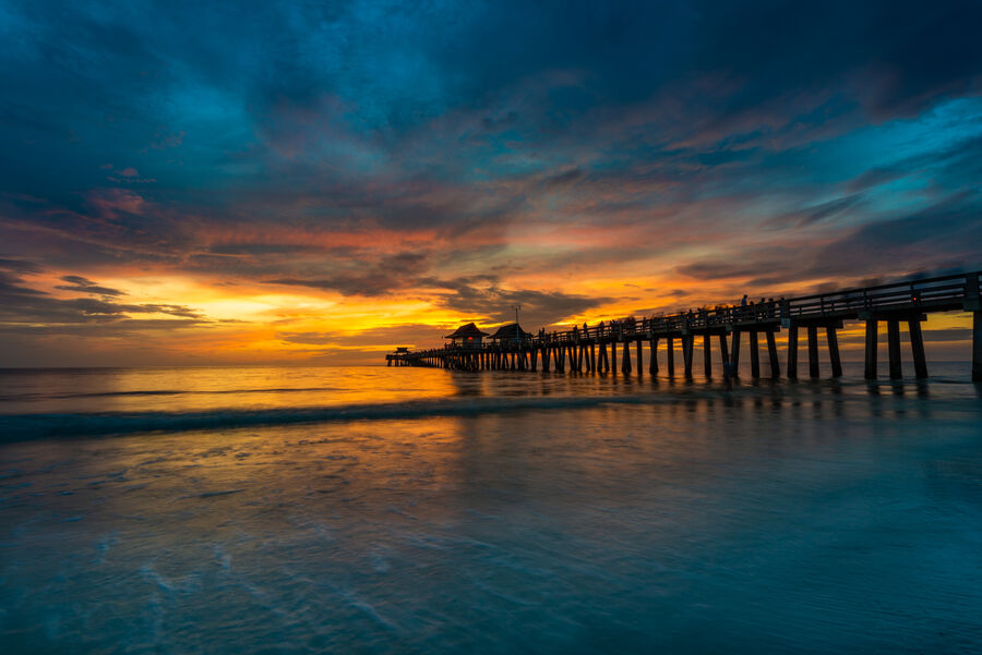 Fine art landscape print of Naples Pier at sunset, the wooden pier extending over the Gulf of Mexico as warm light turns the water to copper
