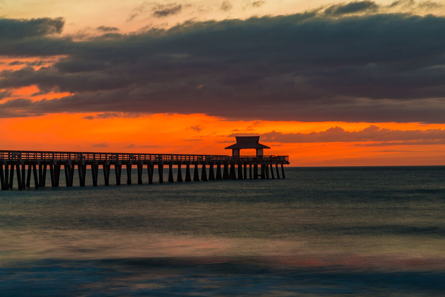 Fine art print of Naples Pier at nautical twilight, dock lights beginning to glow as the sky transitions from orange to deep indigo above the Gulf