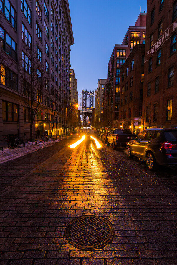 Fine art photograph of Dumbo, Brooklyn at night, the Manhattan Bridge arch framing the Empire State Building perfectly in the gap between buildings